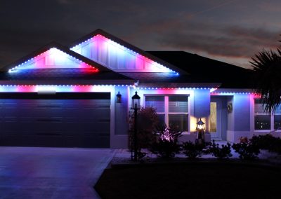 Trimlight 3L permanent roofline lighting in red, white and blue on a home in The Villages, Florida at dusk